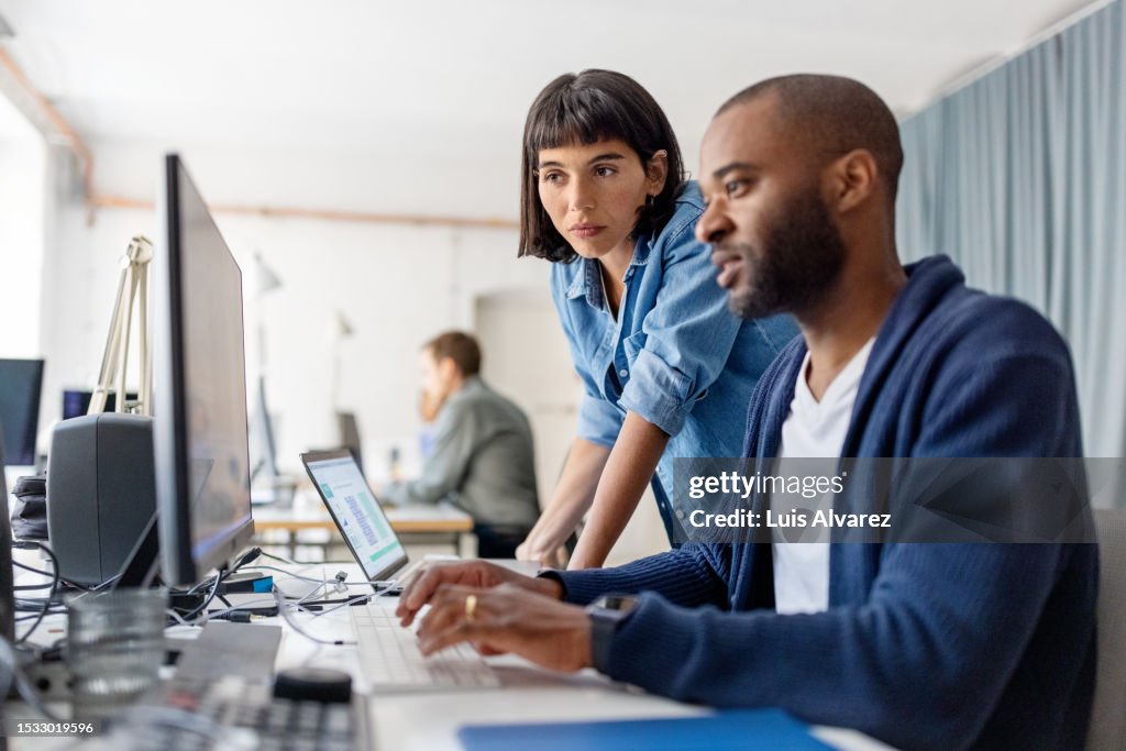 Two businesspeople looking at desktop computer monitor and discussing work at desk