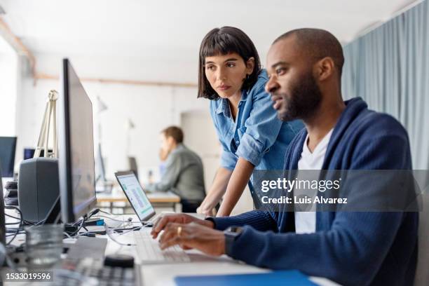 two businesspeople looking at desktop computer monitor and discussing work at desk - computer programmer desk stock pictures, royalty-free photos & images