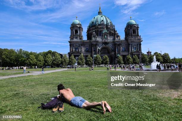 Man sun bathes on the lawn as people cool off in a fountain in front of Dom cathedral on July 15, 2023 in Berlin, Germany. Weather forecasts are...