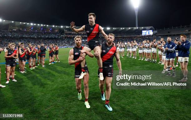 Zach Merrett of the Bombers is chaired from the field after his 200th match by teammates Dyson Heppell and Jake Stringer during the 2023 AFL Round 18...