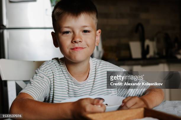 little boy having breakfast in the kitchen and looking at camera - breakfast bowl stock pictures, royalty-free photos & images