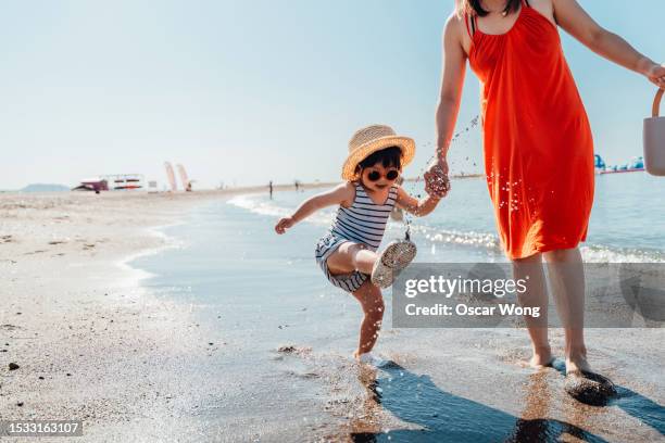 cute asian little girl kicking water while walking with her mother on the beach - kicking sand stock pictures, royalty-free photos & images