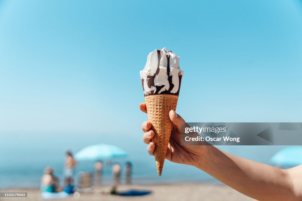 Female hand holding ice-cream on the beach against clear blue sky