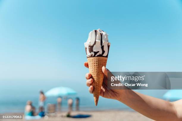 female hand holding ice-cream on the beach against clear blue sky - hot spanish women fotografías e imágenes de stock