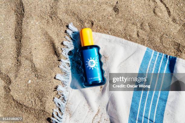 elevated view of sun cream and beach towel in sand on a sunny day - sonnencreme stock-fotos und bilder