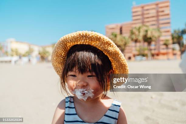 portrait of cute asian little girl eating ice-cream on the beach - girl eating messy ice cream cone stock-fotos und bilder