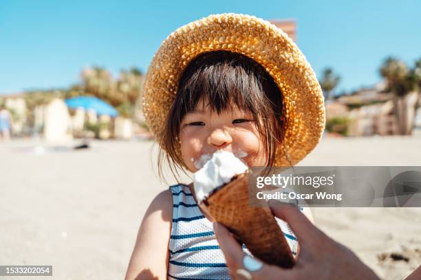 portrait of cheerful asian little girl eating ice-cream on the beach - girl eating messy ice cream cone stock-fotos und bilder