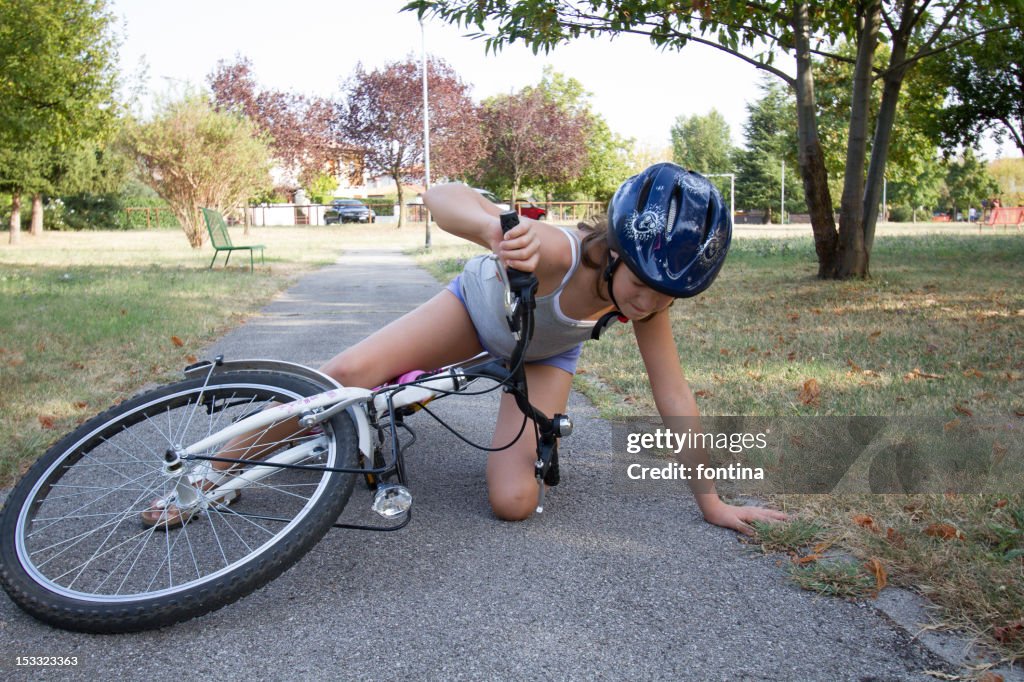 Girl wearing helmet and fallen with her bike