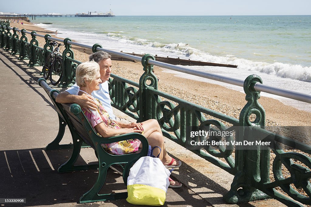 Senior couple sitting on bench looking at sea.