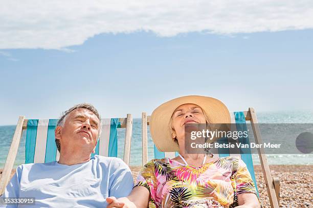 senior couple relaxing in deckchairs on beach. - man on the beach relaxing in deckchair fotografías e imágenes de stock