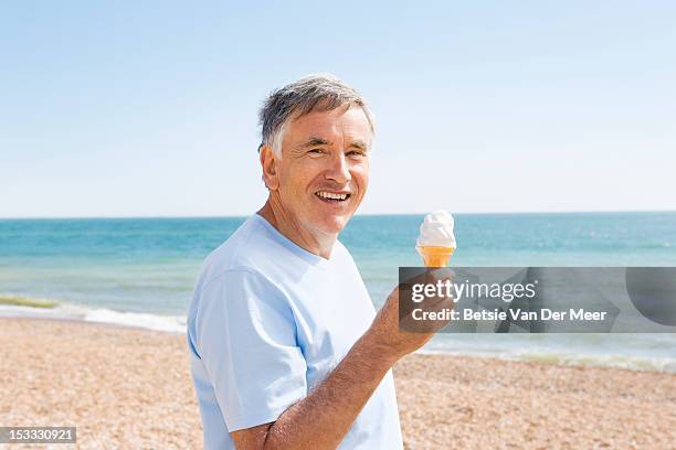 senior man holding icecream standing on beach. - senior men eating stock pictures, royalty-free photos & images