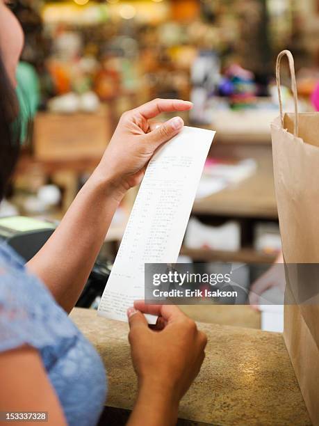 mixed race woman looking at shopping receipt - receipts stockfoto's en -beelden