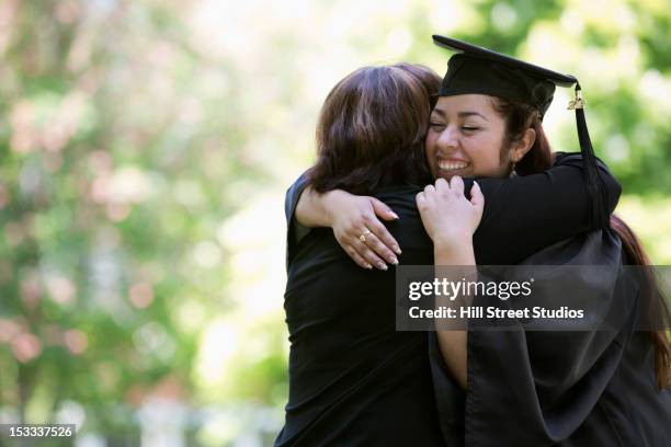 hispanic mother hugging college graduate daughter - graduates stockfoto's en -beelden
