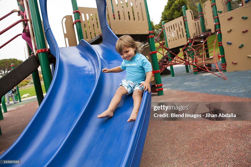 Mixed race boy sliding down slide on playground