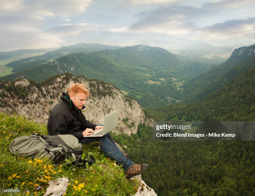 Caucasian man using laptop on remote cliff's edge