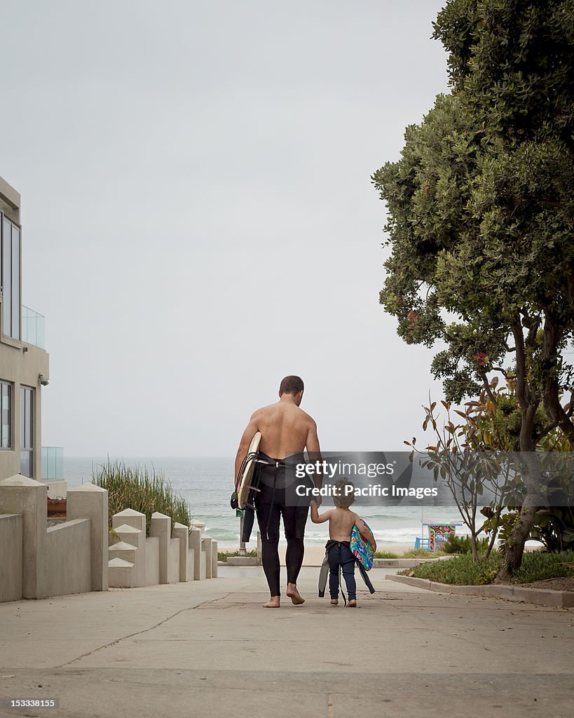 Caucasian father and son in wetsuits walking toward the ocean