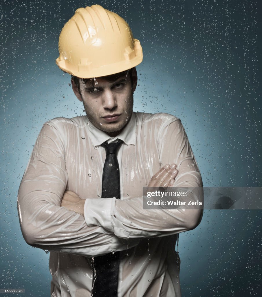 Caucasian businessman in hard-hat standing in rain