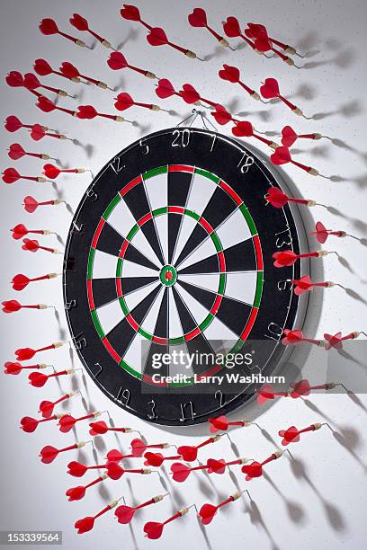 multiple darts stuck in a wall all around a dartboard - off target stockfoto's en -beelden