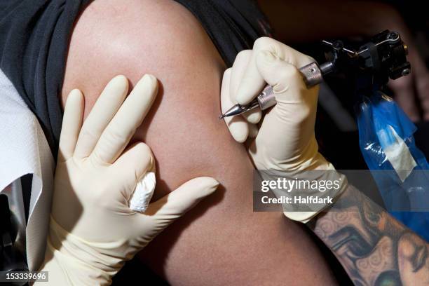 a tattoo artist preparing to tattoo a man's bare arm, close-up - tatouage stockfoto's en -beelden