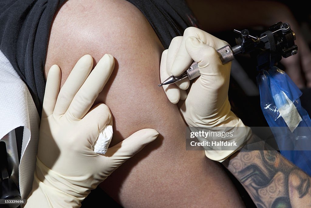 A tattoo artist preparing to tattoo a man's bare arm, close-up