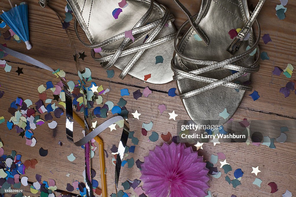 Metallic strappy heels, confetti and streamers littering a hardwood floor