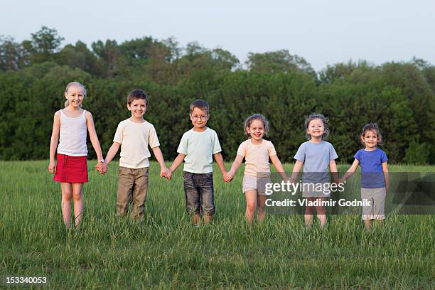 portrait of children holding hands in a field - child development stock pictures, royalty-free photos & images