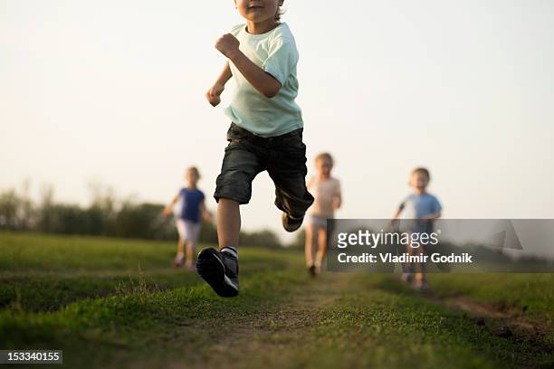 low view of a boy running in a field with other children behind - bambini che corrono foto e immagini stock