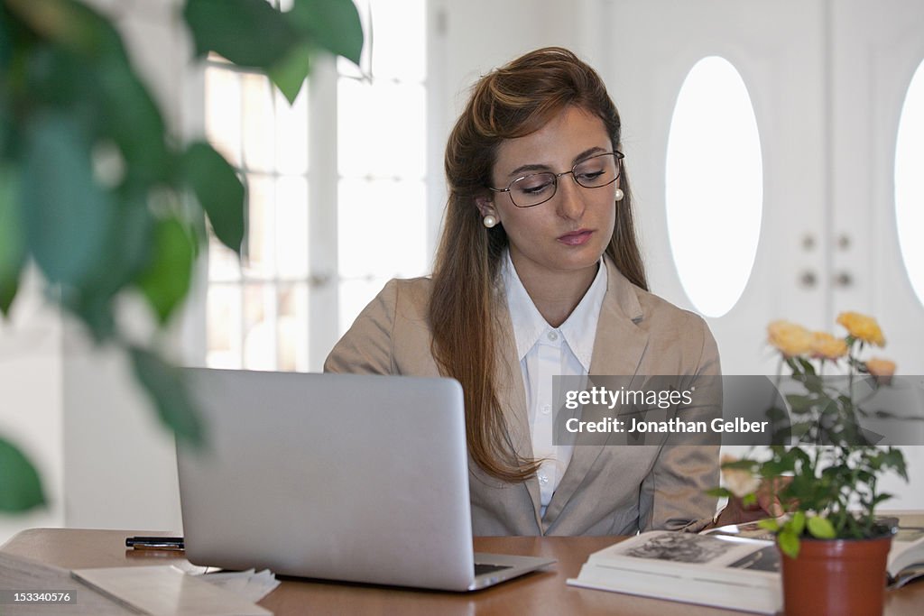 A businesswoman using a laptop and reading a book at her office desk