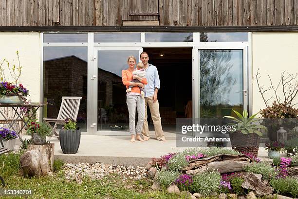 a man and a woman holding a baby standing on the patio in front of their house - family in front of house stockfoto's en -beelden