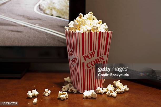 a red striped carton of popcorn on a table in front of a flat screen tv - parte de uma série - fotografias e filmes do acervo