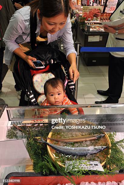 Mother and a baby admire a golden saury and an ordinary silver-coloured saury at the fish shop of the Seibu department store in Tokyo on October 4,...