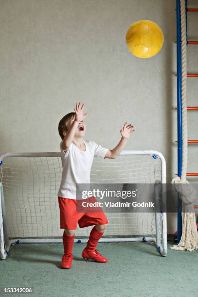 a young boy defending a goal while a ball flies towards him - boy goalie standing in front of goal net stock pictures, royalty-free photos & images