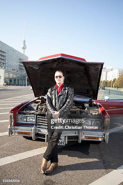 a cool rockabilly guy holding tools leaning against the front of his vintage car, hood up - rockabilly stock-fotos und bilder