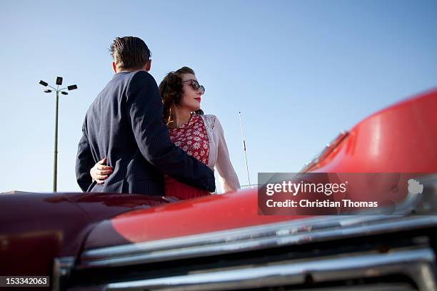 a cool, rockabilly couple with arms around each other by a vintage car - rockabilly pin up girls stock pictures, royalty-free photos & images