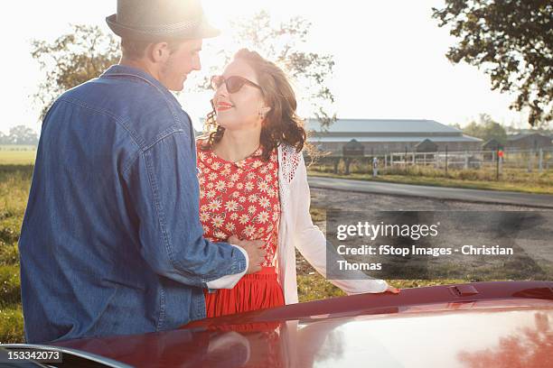 a flirtatious rockabilly couple standing next to a vintage car - rockabilly pin up girls stock pictures, royalty-free photos & images