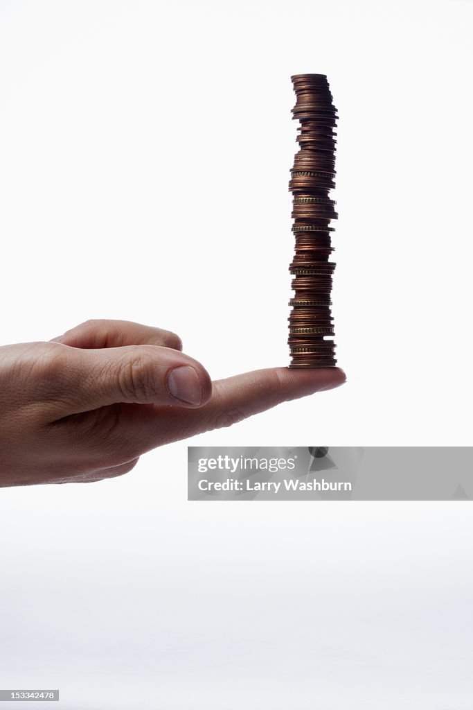 A human finger balancing a stack of various Euro coins, close-up