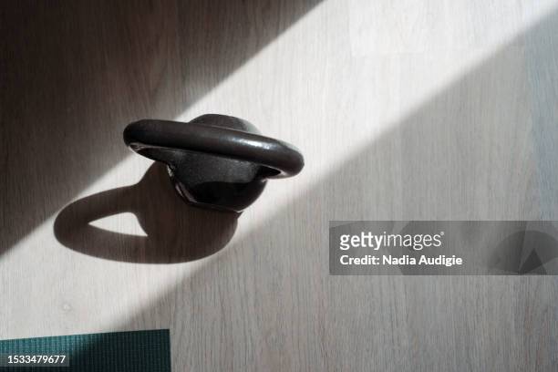 black kettlebell on a hardwood floor in a sun ray next to yoga mat - kettle bell stock pictures, royalty-free photos & images