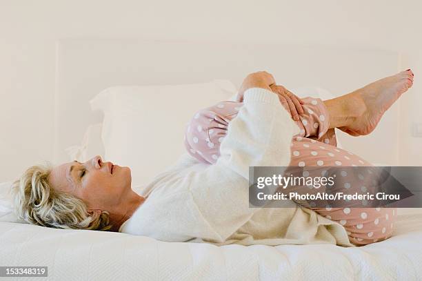 mature woman lying on bed in fetal position - foetushouding stockfoto's en -beelden