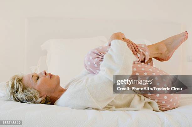 mature woman lying on bed in fetal position - hugging knees - fotografias e filmes do acervo