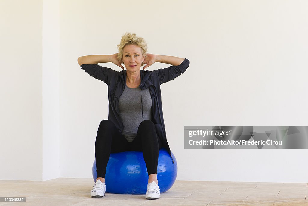 Mature woman sitting on fitness ball with hands behind head