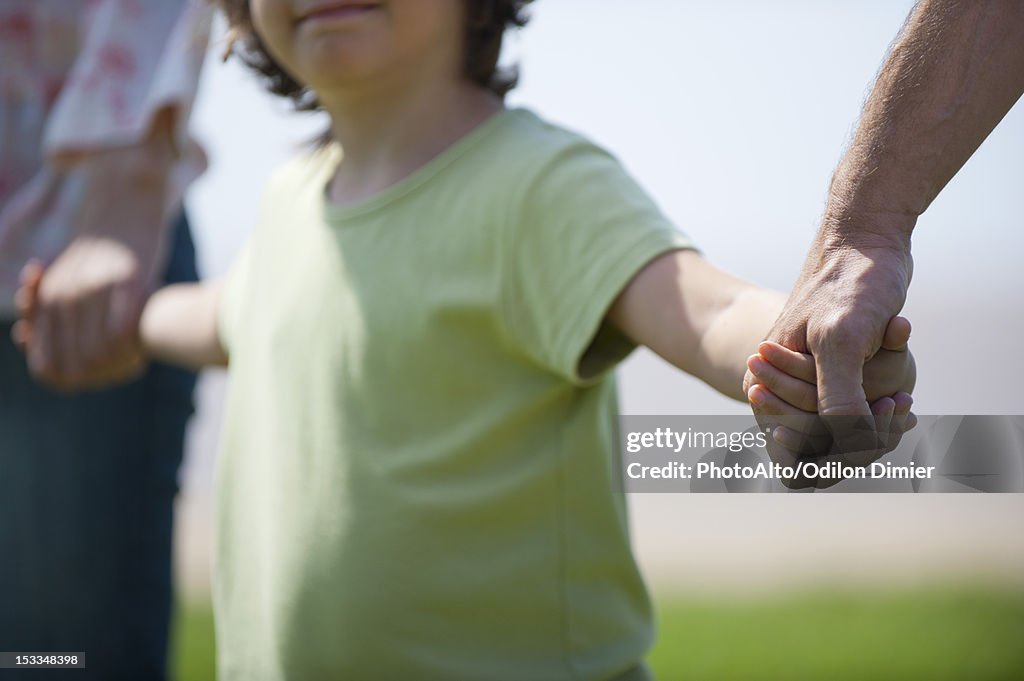 Boy holding hands with parents, cropped