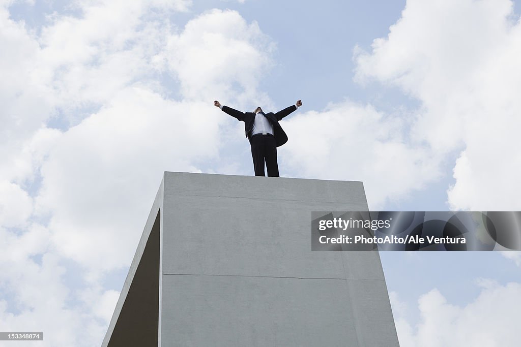 Businessman standing on concrete structure with arms outstretched, low angle view