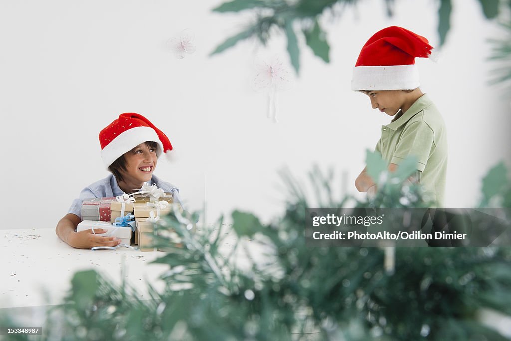 Boy holding armful of Christmas presents, smiling mischievously at sulky brother