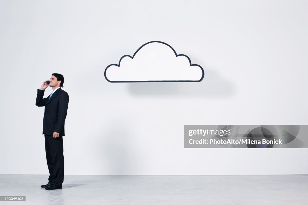 Businessman talking on cell phone near graphic cloud representing cloud computing