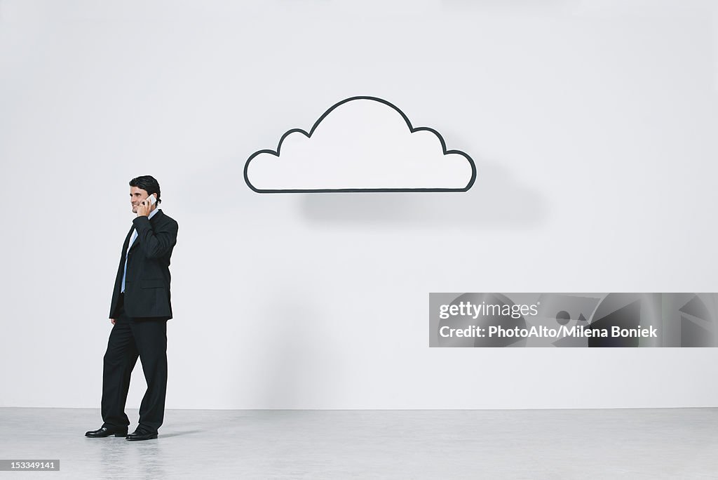 Businessman talking on cell phone near graphic cloud representing cloud computing