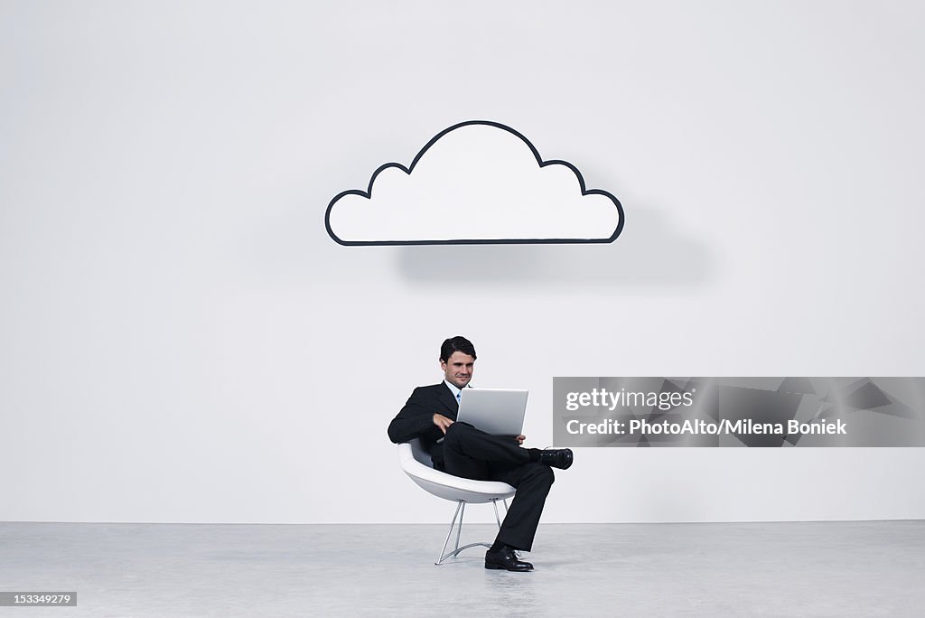 Businessman using laptop computer beneath cloud representing cloud computing