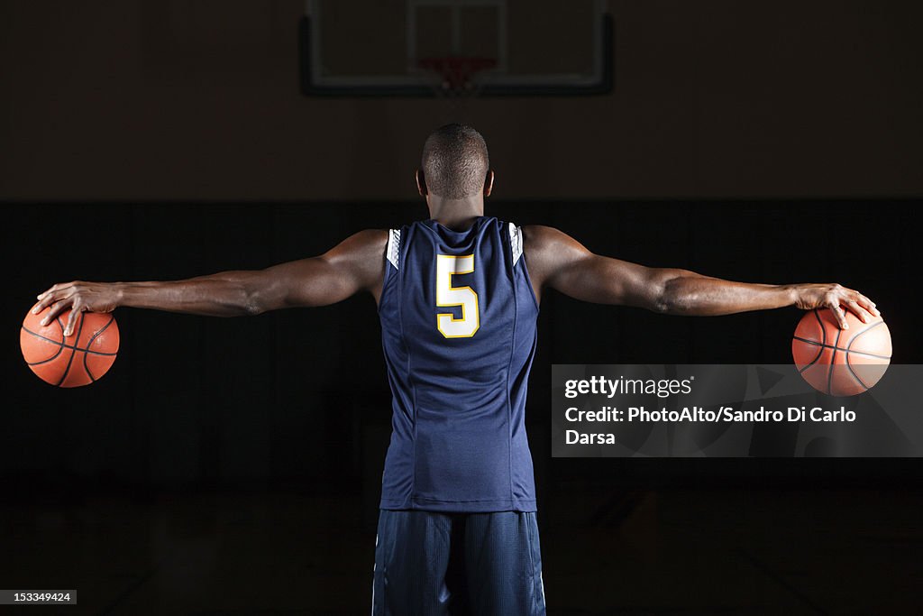 Basketball player holding basketballs in both hands, rear view