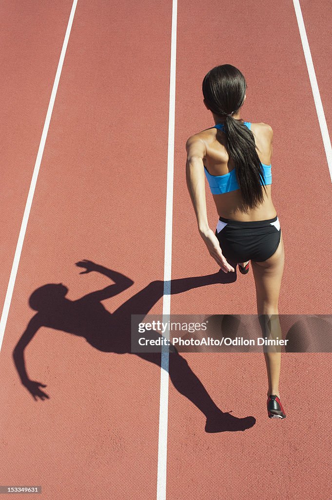 Female athlete running on track, focus on shadow