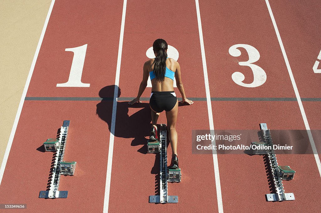 Female athlete in starting position on running track, rear view