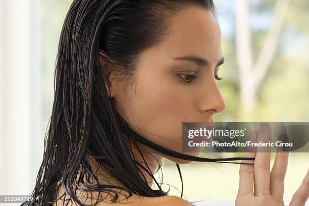 woman looking at strand of hair, side view - hand in hair foto e immagini stock